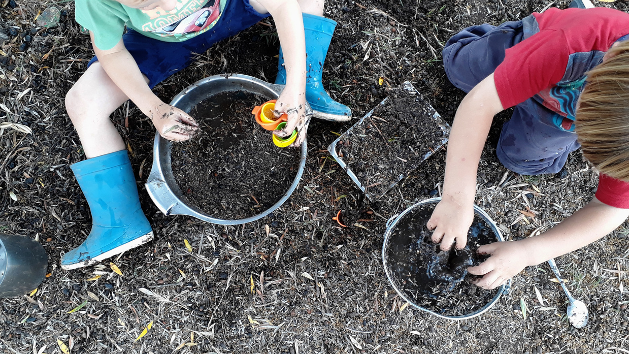 Children exploring with muddy hands during outdoor learning time