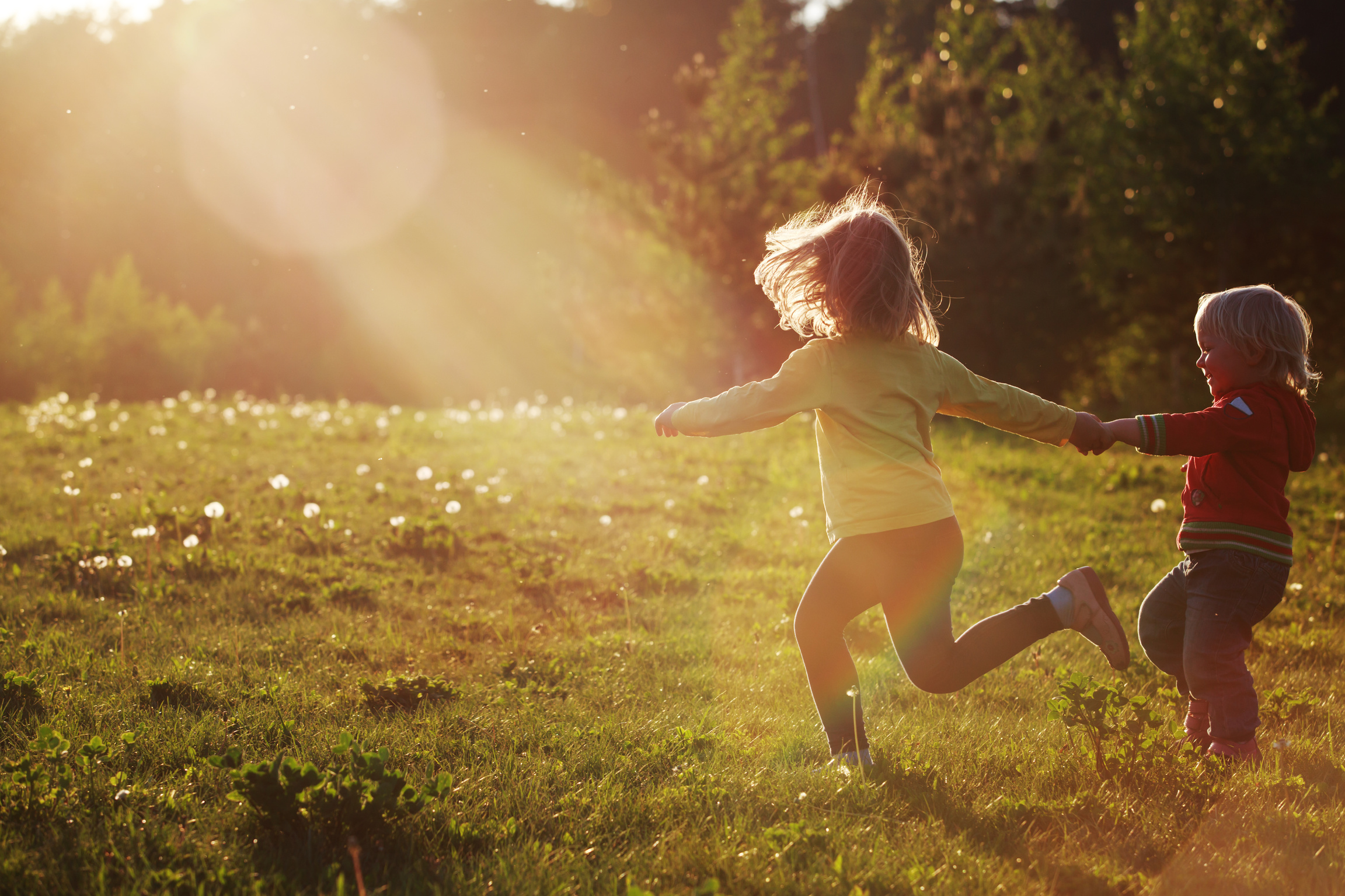 Two children joyfully running hand in hand through a sunlit meadow